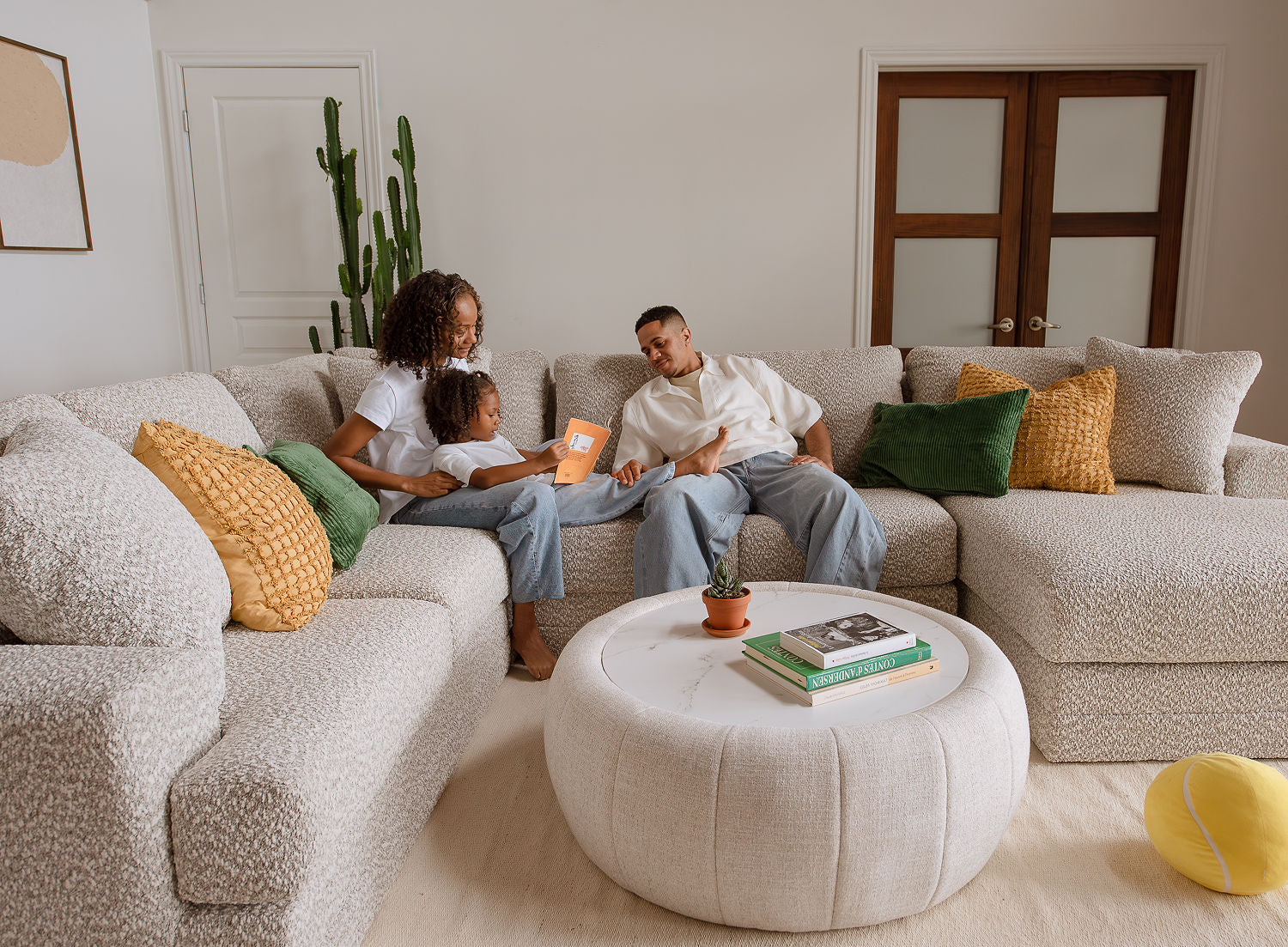 Famille assise sur un sofa sectionnel beige en tissu bouclé dans un salon lumineux