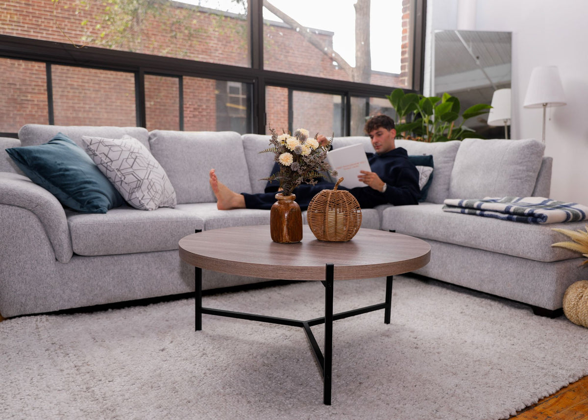 Homme qui lit, confortablement installé sur un sofa sectionnel gris pâle, table basse ronde en bois