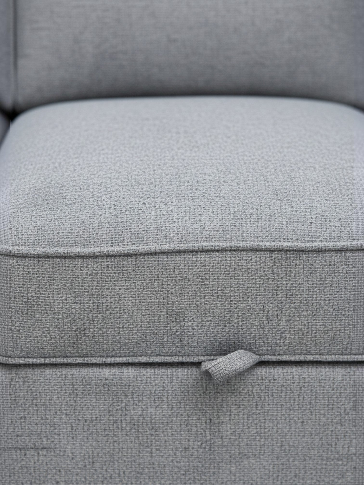 Gros plan sur le tissu gris texturé du canapé-lit Amani de TOCO Meubles avec sa languette de déploiement