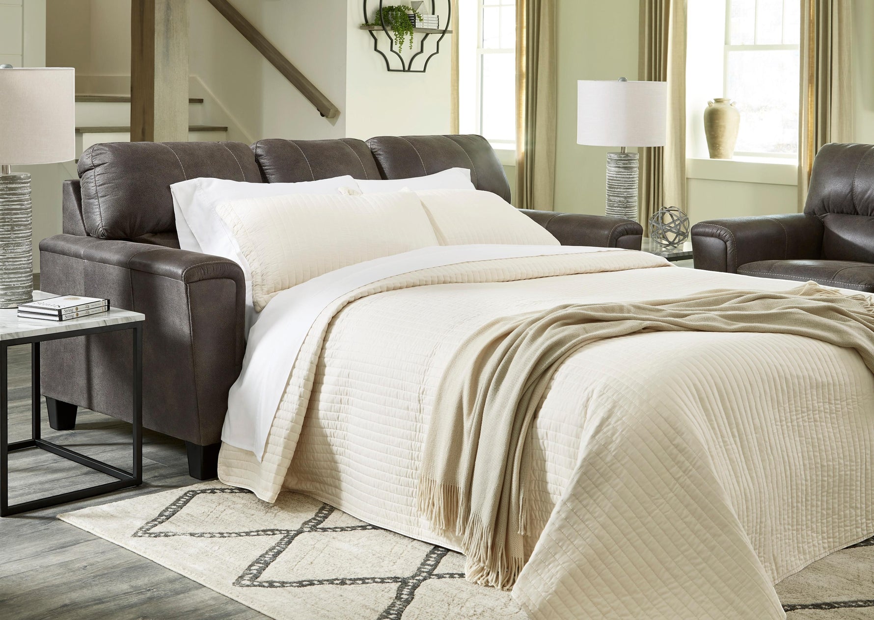 TOCO Meubles Canapé-lit Kairo marron en aspect cuir, convertible en lit, avec couette crème et jeté de lit beige.