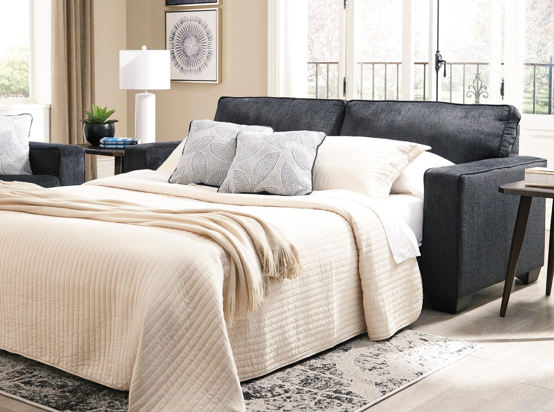 TOCO Meubles - Canapé-lit Marcel bleu foncé, tissu texturé, avec couette beige matelassée et coussins décoratifs.