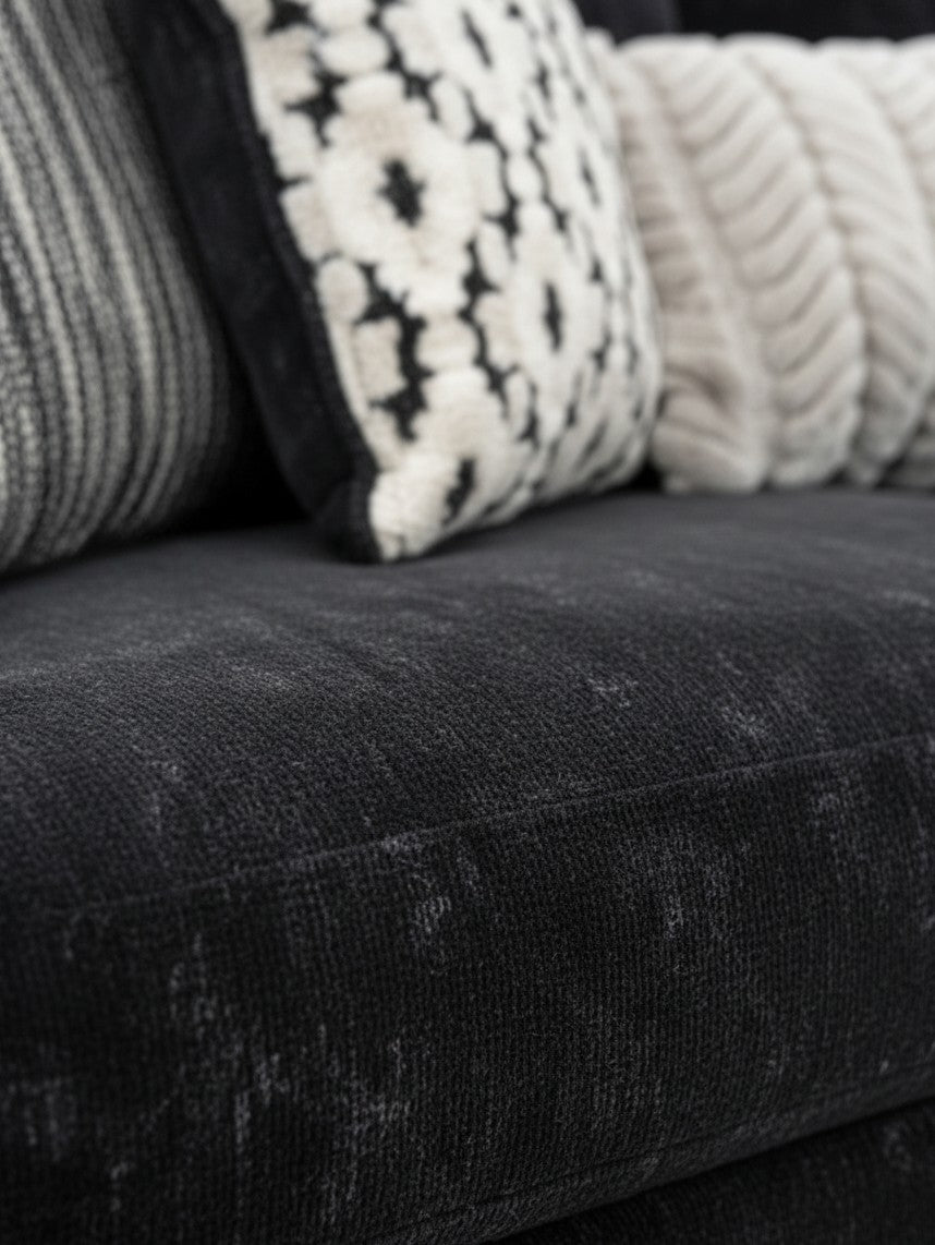Gros plan sur le canapé Mistral de TOCO Meubles en tissu noir texturé avec coussins décoratifs à motifs
