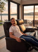 Homme assis sur une causeuse inclinable en cuir noir TOCO Meubles dans un salon moderne avec vue sur le lac
