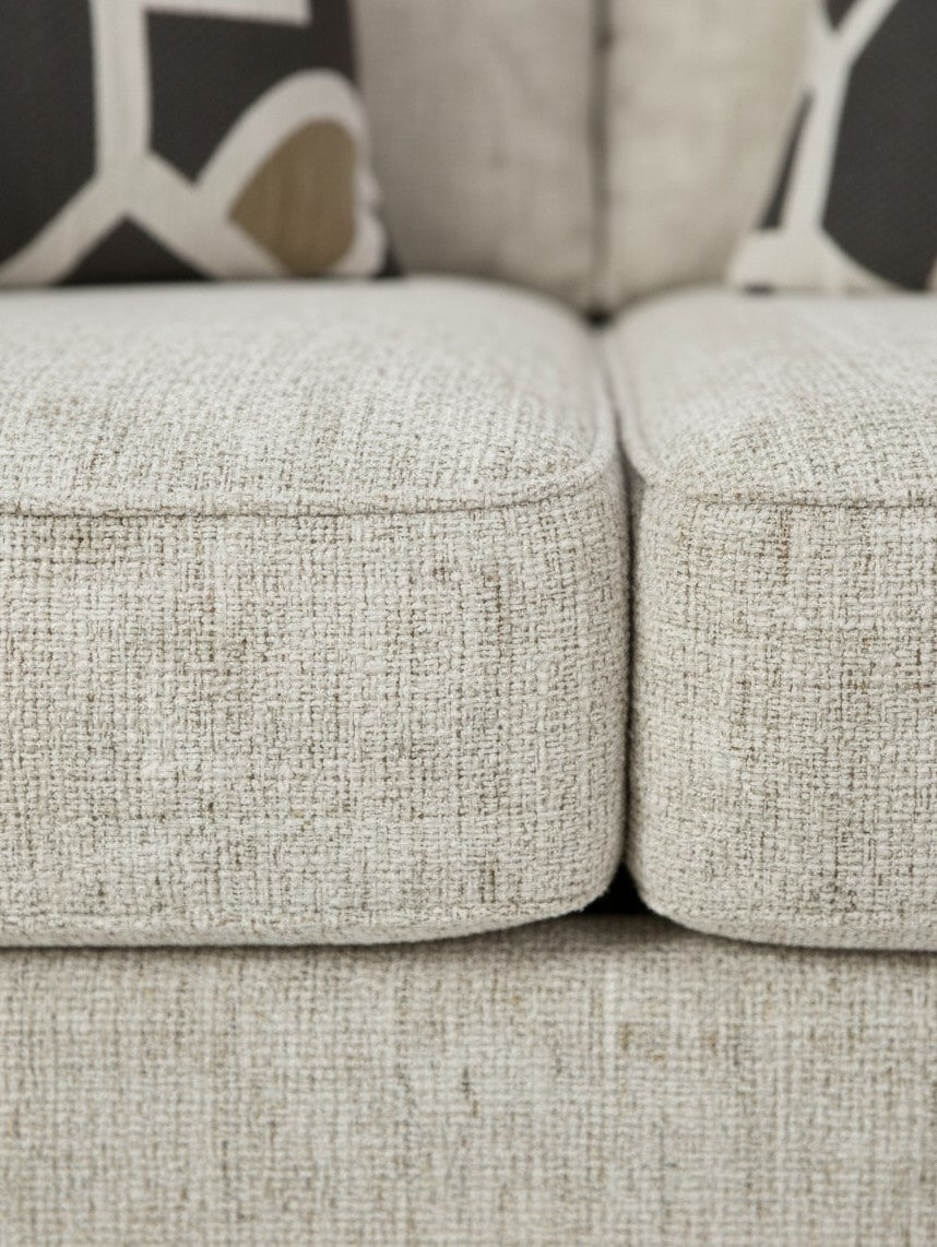Gros plan sur le tissu texturé beige de la causeuse Moka de TOCO Meubles avec coussins décoratifs à motifs