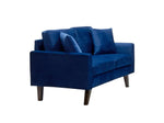 Causeuse Royal bleue en velours de TOCO Meubles, avec coussins assortis et pieds en bois foncés.