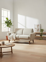 Causeuse Tano de TOCO Meubles en tissu beige clair avec pieds en bois dans un salon lumineux au style scandinave