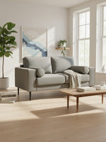 Causeuse Zela TOCO Meubles en tissu gris anthracite avec coussins cylindriques dans un salon moderne et lumineux