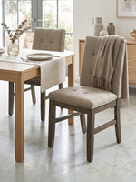 Chaise de cuisine TOCO Meubles Véronika en tissu brun capitonné avec structure en bois massif gris dans une salle à manger
