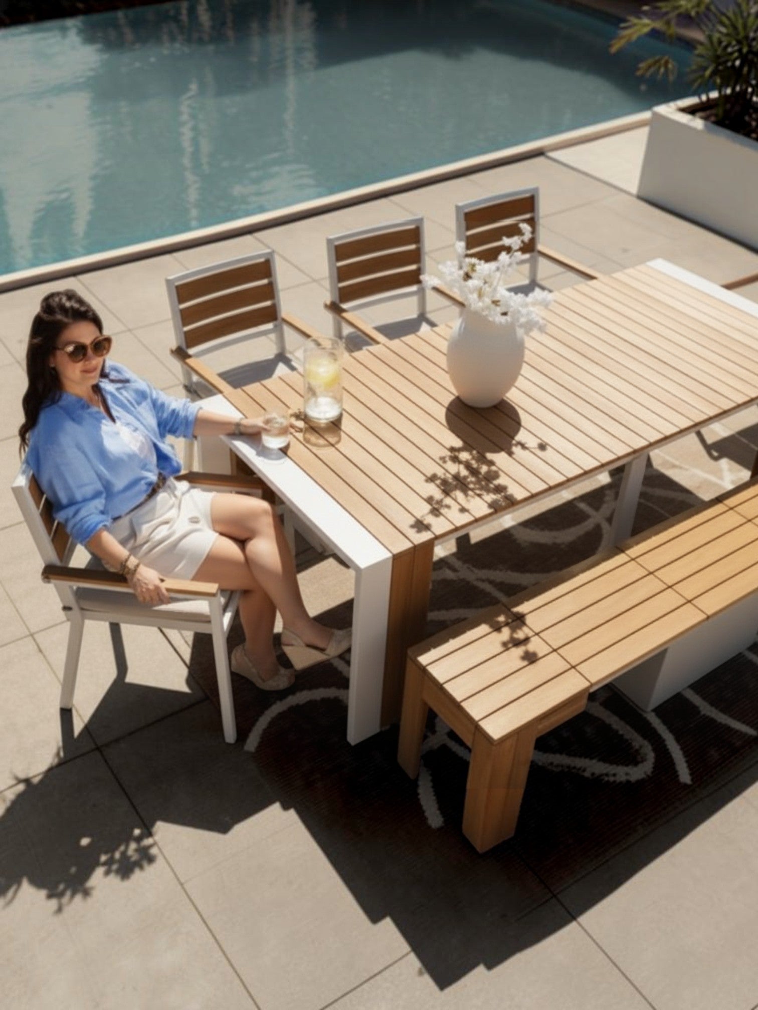 Femme assise sur une chaise d'extérieur TOCO Meubles en bois et métal blanc près d'une piscine ensoleillée