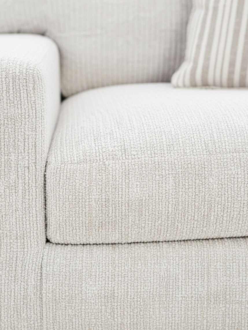 Gros plan sur le tissu texturé beige clair de la chaise Figaro de TOCO Meubles avec un coussin rayé assorti