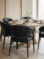 Chaise de salle à manger Bronso TOCO Meubles en similicuir noir avec dossier courbé autour d'une table ronde en bois