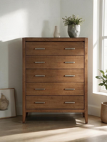 Commode haute Antoine de TOCO Meubles en bois brun clair brossé avec cinq tiroirs et poignées en laiton antique.