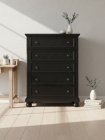 Commode haute Margaux de TOCO Meubles en bois noir effet usé avec cinq tiroirs et pieds boule dans une chambre