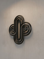 Décoration murale TOCO Meubles Aurum en métal noir aux formes géométriques arrondies sur un mur gris texturé