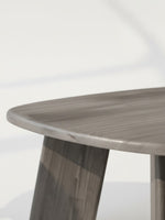 Gros plan sur le plateau arrondi et les pieds en bois gris de l'ensemble de tables Hina par TOCO Meubles