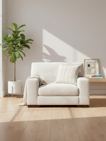 Fauteuil TOCO Meubles Figaro en tissu texturé blanc cassé avec coussin rayé et plaid dans un salon lumineux