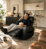 Homme relaxé dans un fauteuil inclinable noir TOCO Meubles en cuir avec surpiqûres dans un salon moderne.