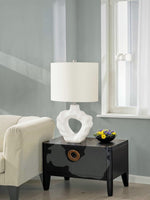 Lampe de table TOCO Meubles Belo avec base sculpturale blanche en résine et abat-jour en lin sur une table noire