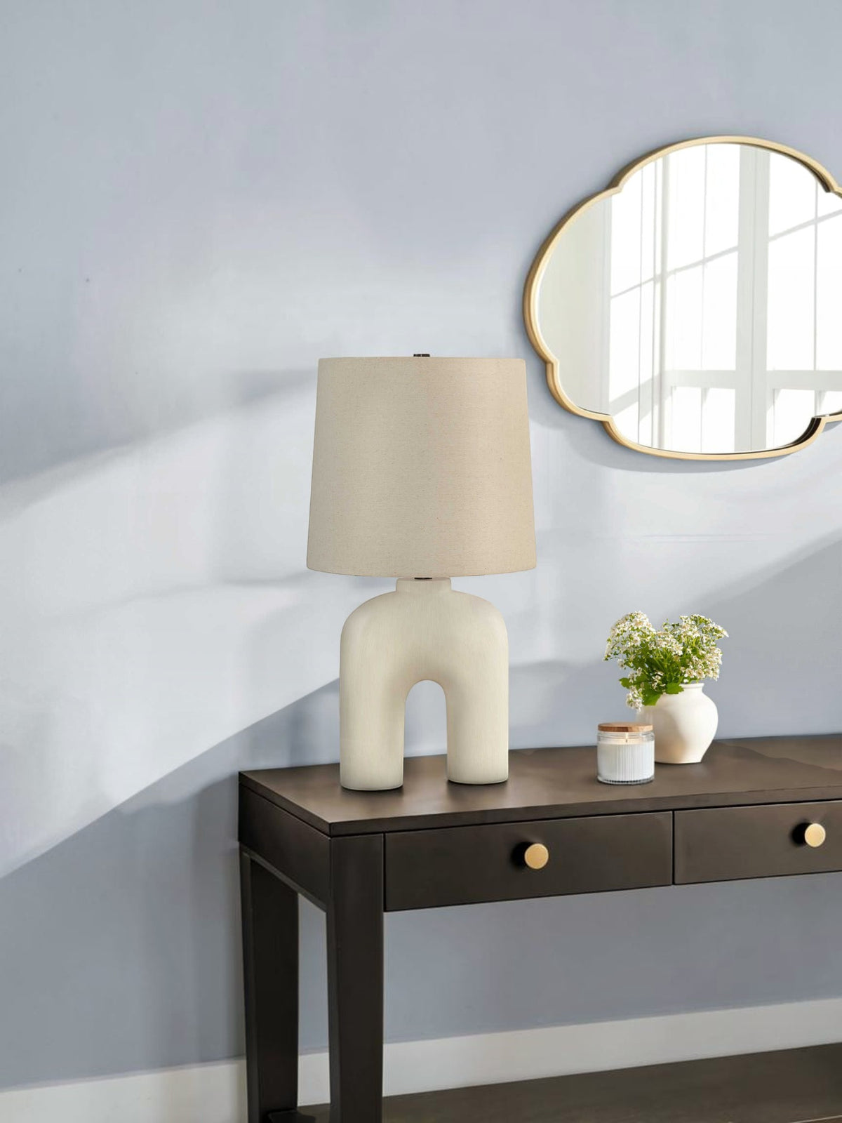 Lampe de table TOCO Meubles Pedro avec base sculpturale en arche et abat-jour en lin beige sur une console sombre