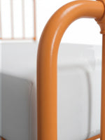 Gros plan sur la structure en métal orange du lit Daisy de TOCO Meubles avec ses courbes arrondies élégantes.