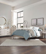 Lit double Solene TOCO Meubles en bois clair avec couvre-lit bleu matelassé et coussins décoratifs.