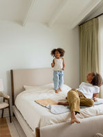 Lit plateforme TOCO Meubles Zavian en tissu chenille beige avec montants en bois chêne dans une chambre lumineuse