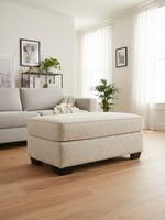 Ottoman Moka de TOCO Meubles en tissu texturé beige clair avec pieds en bois foncé dans un salon lumineux