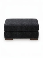 Ottoman Mistral de TOCO Meubles en tissu texturé gris foncé avec pieds en bois massif sur fond blanc