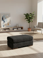 Ottoman Mistral de TOCO Meubles en tissu gris anthracite avec base en bois dans un salon moderne et lumineux