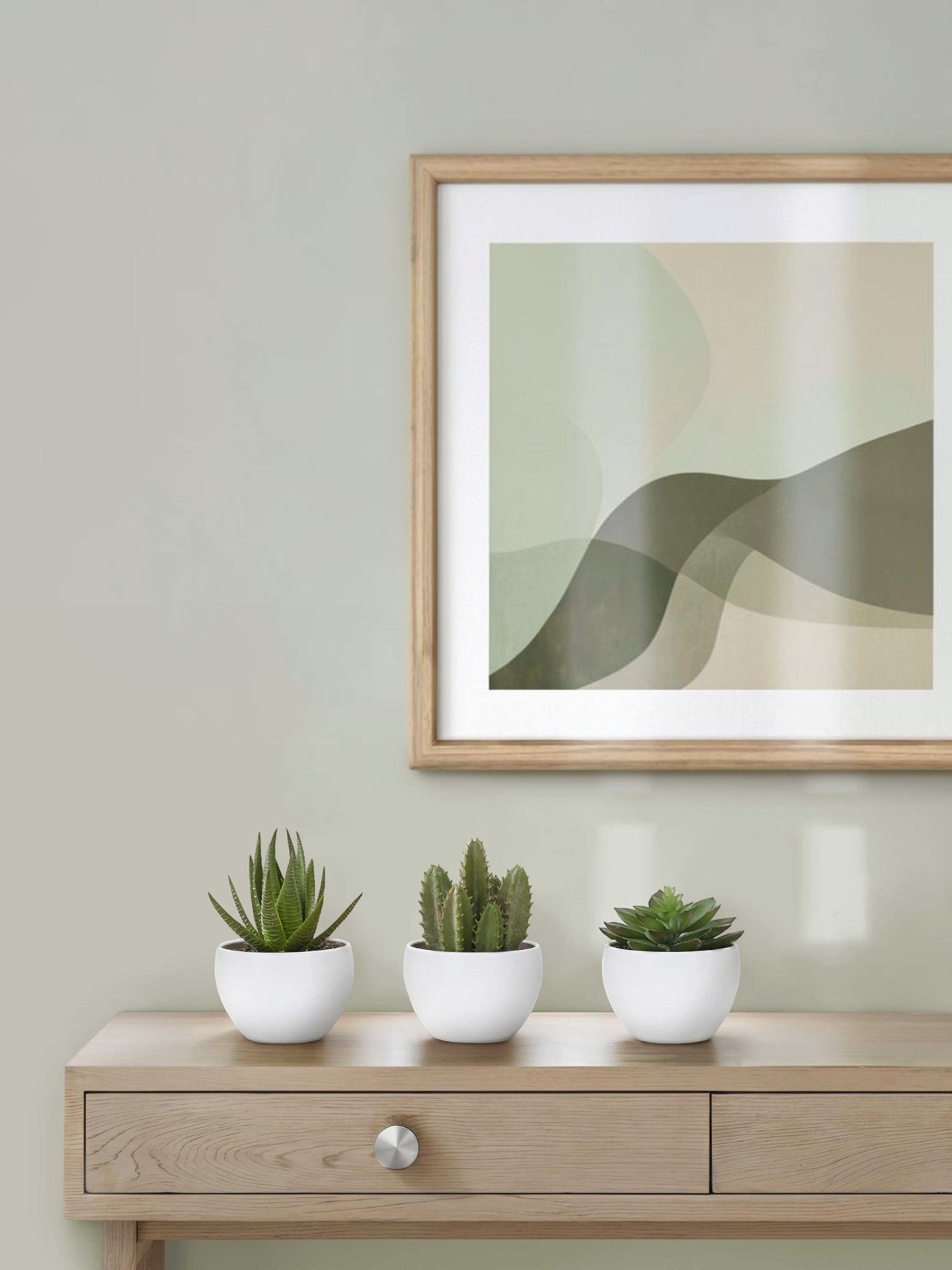 Trois petites plantes artificielles TOCO Meubles dans des pots blancs sur une console en bois sous un cadre abstrait