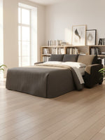 Sofa-lit Muna de TOCO Meubles en tissu gris foncé, transformé en lit dans un salon lumineux et contemporain.
