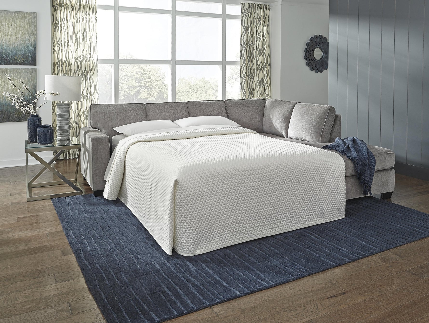 TOCO Meubles Sofa-lit sectionnel Marcel gris en tissu, transformable en lit, avec couette blanche matelassée.