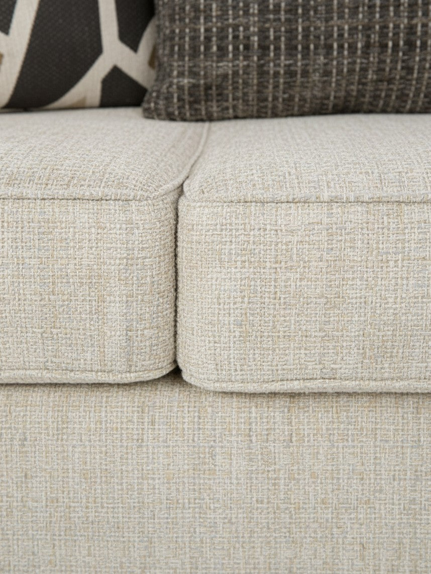 Gros plan sur le tissu texturé beige du canapé Moka de TOCO Meubles avec des coussins décoratifs contrastés