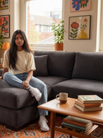 Jeune femme assise sur un sofa sectionnel gris en velours côtelé TOCO Meubles dans un salon au style bohème.