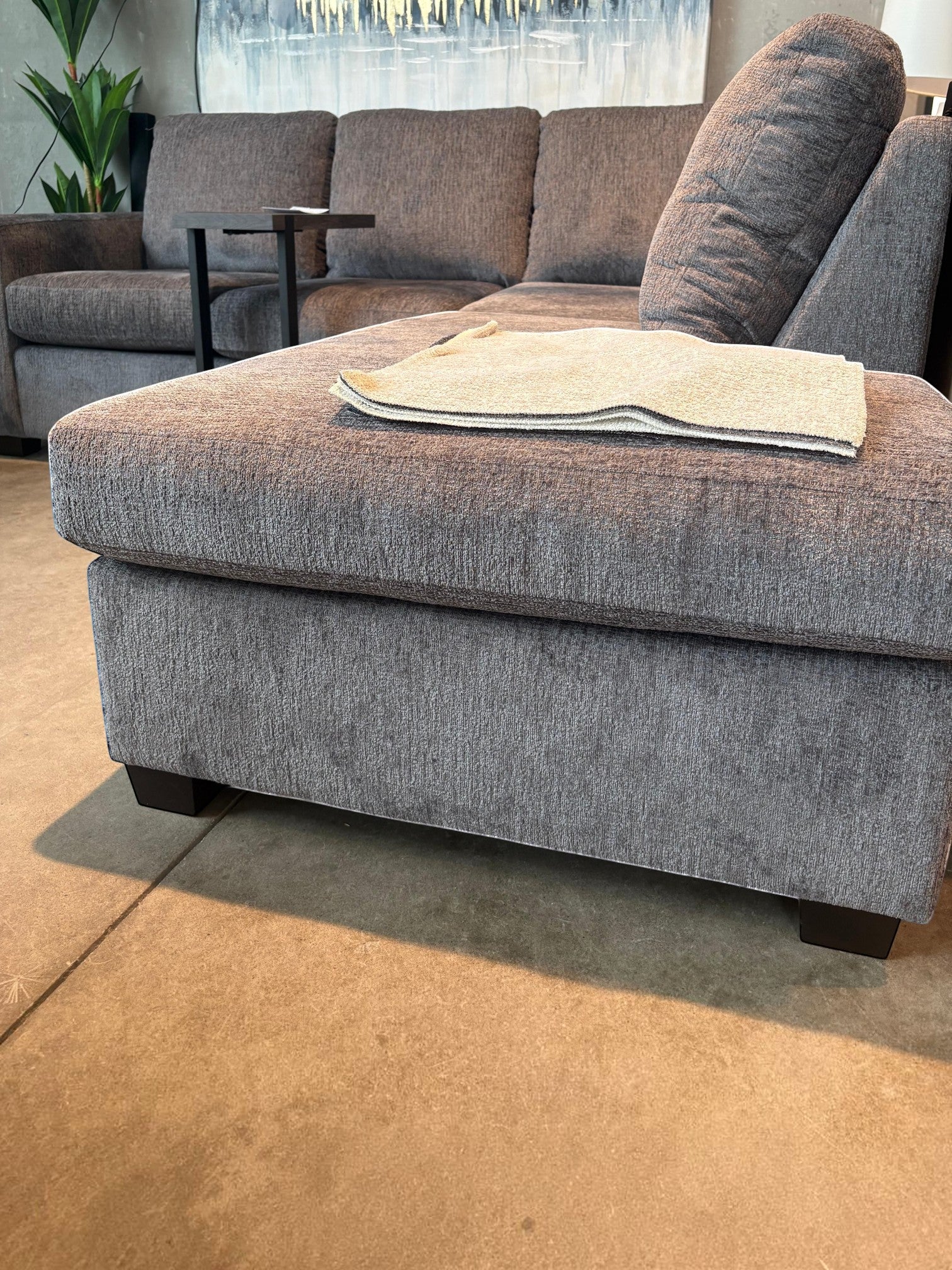 Sofa sectionnel gris TOCO Meubles modèle Colonel avec pouf assorti et texture en tissu dans un salon moderne