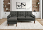 TOCO Meubles Sofa sectionnel Khamo gris foncé capitonné avec repose-pieds et coussins cylindriques sur tapis blanc.
