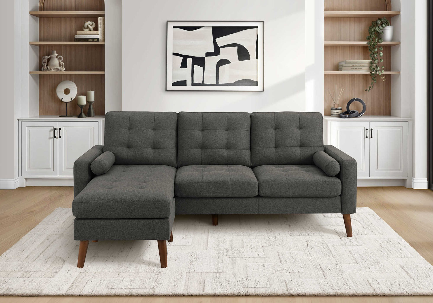 TOCO Meubles Sofa sectionnel Khamo gris foncé capitonné avec repose-pieds et coussins cylindriques sur tapis blanc.
