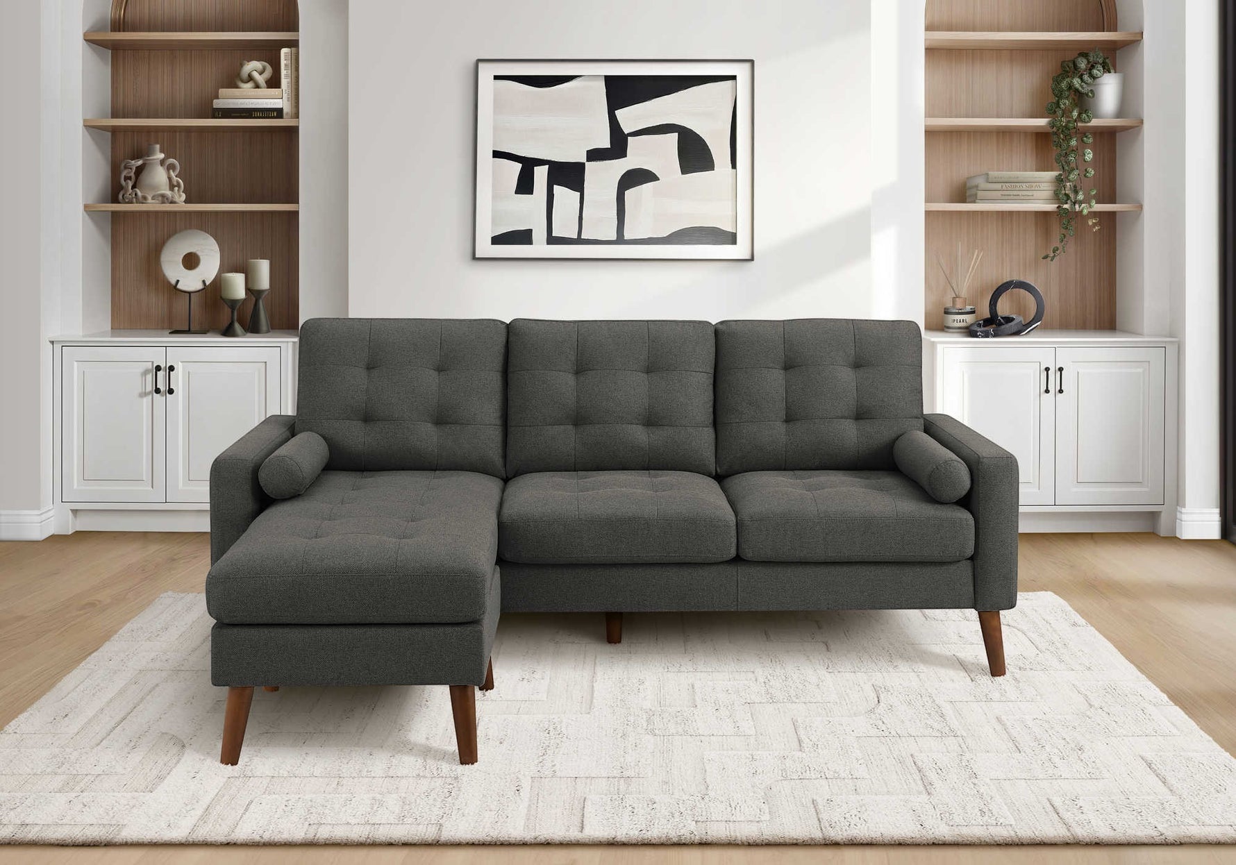 TOCO Meubles Sofa sectionnel Khamo gris foncé capitonné avec repose-pieds et coussins cylindriques sur tapis blanc.
