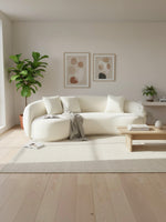 Sofa Swayn TOCO Meubles incurvé en velours bouclé blanc crème avec coussins dans un salon moderne et lumineux