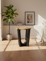 Table d'appoint Annie TOCO Meubles ronde avec plateau en bois naturel et base géométrique noire dans un salon moderne