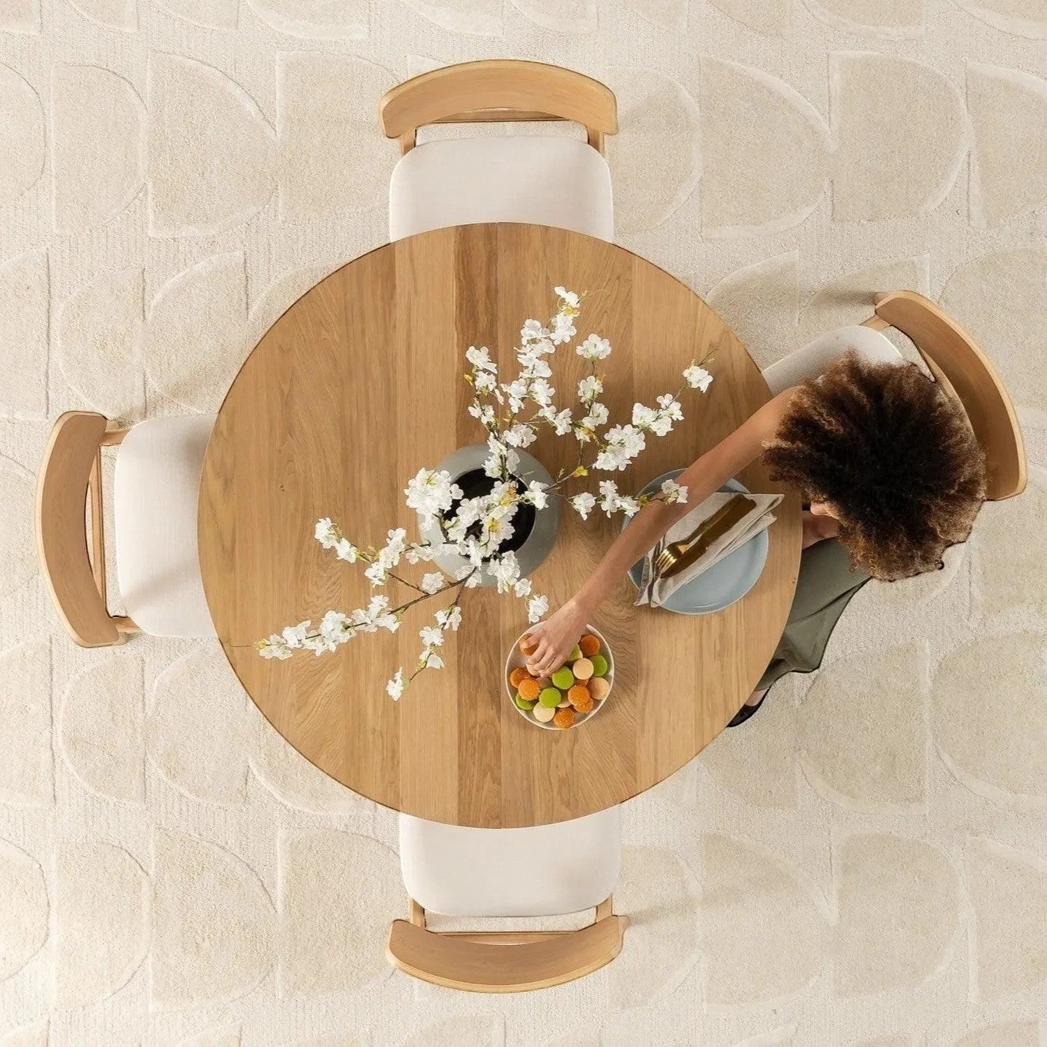 Table de salle à manger TOCO Meubles en chêne scandinave, ronde, avec 4 chaises blanches et un vase de fleurs blanches.
