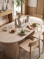 Table de cuisine TOCO Meubles Kamilia ovale en bois clair avec pieds cannelés dans une salle à manger lumineuse