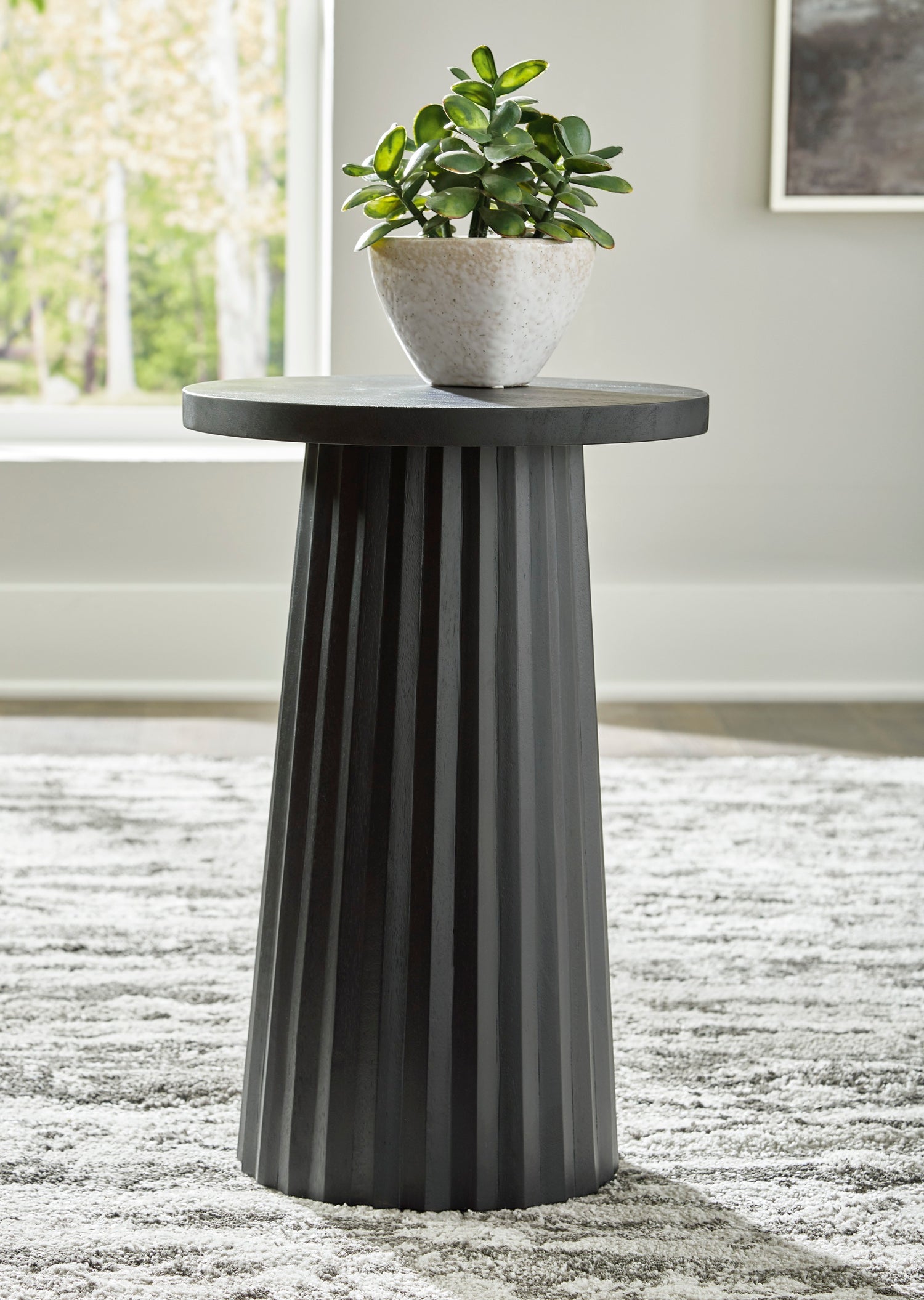 Table d'appoint Ada TOCO Meubles en bois noir avec base cannelée sculpturale et plante verte.