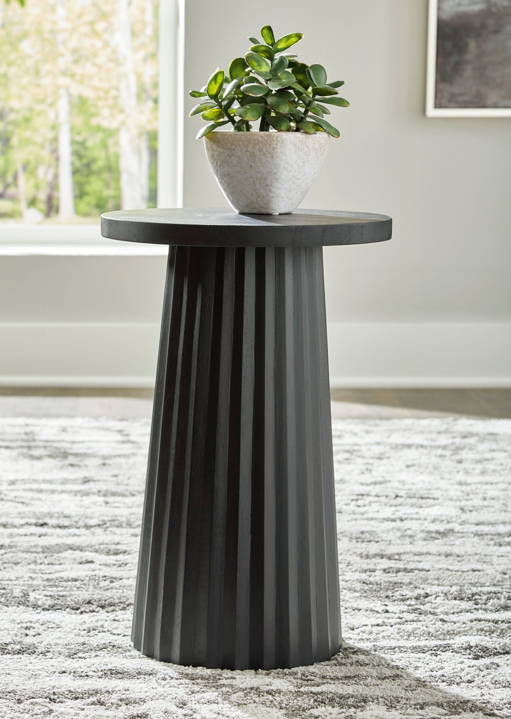 Table d'appoint Ada TOCO Meubles en bois noir avec base cannelée sculpturale et plante verte.