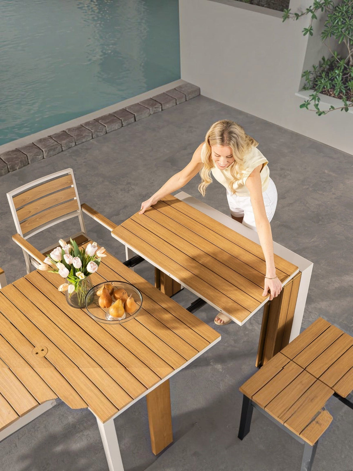 Femme déployant la table à manger extérieure extensible Transformer de TOCO Meubles en bois sur une terrasse moderne