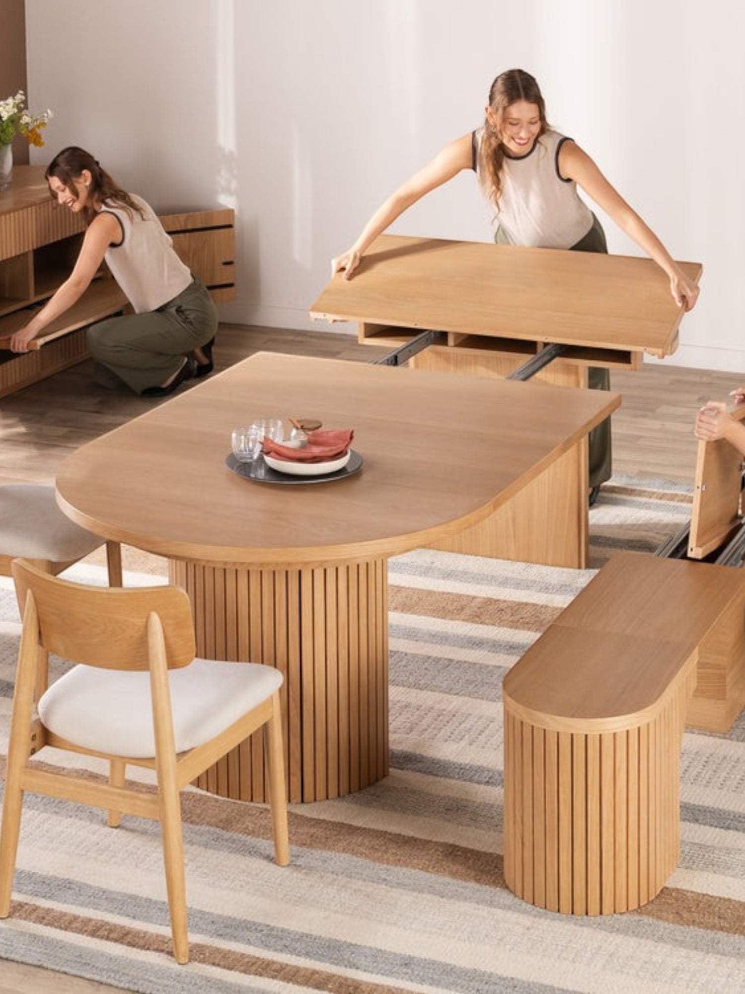 TOCO Meubles Table de salle à manger ronde en chêne scandinave, extensible, avec pieds cannelés et 2 femmes démontrant son mécanisme.