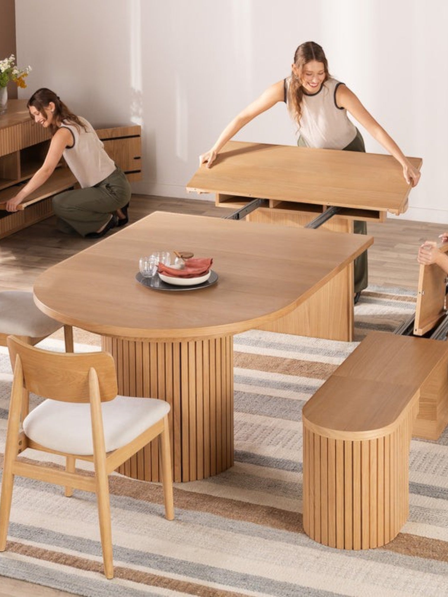 TOCO Meubles Table de salle à manger ronde en chêne scandinave, extensible, avec pieds cannelés et 2 femmes démontrant son mécanisme.