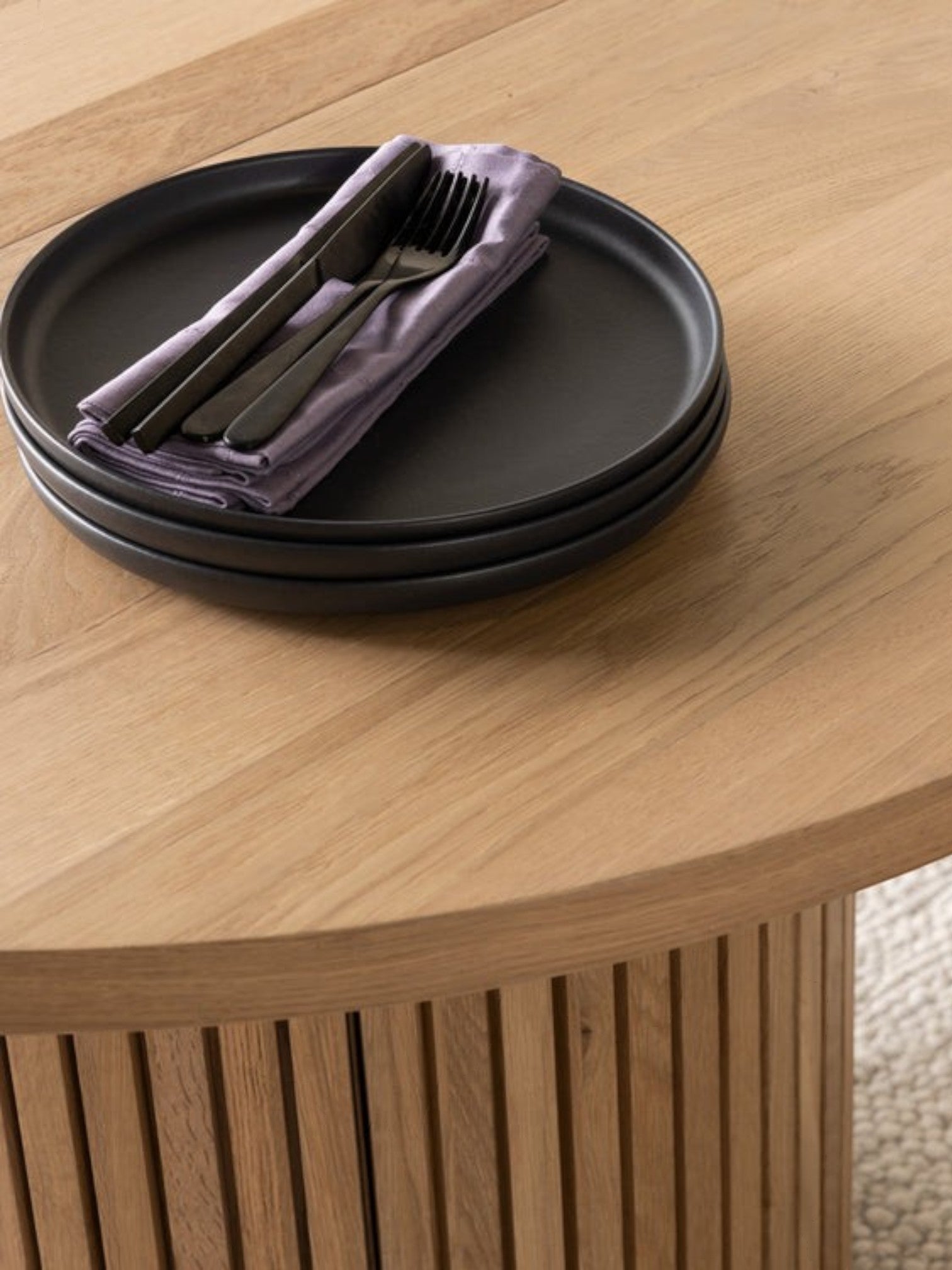 Table de salle à manger ronde en chêne scandinave TOCO Meubles avec pieds cannelés et assiettes noires.