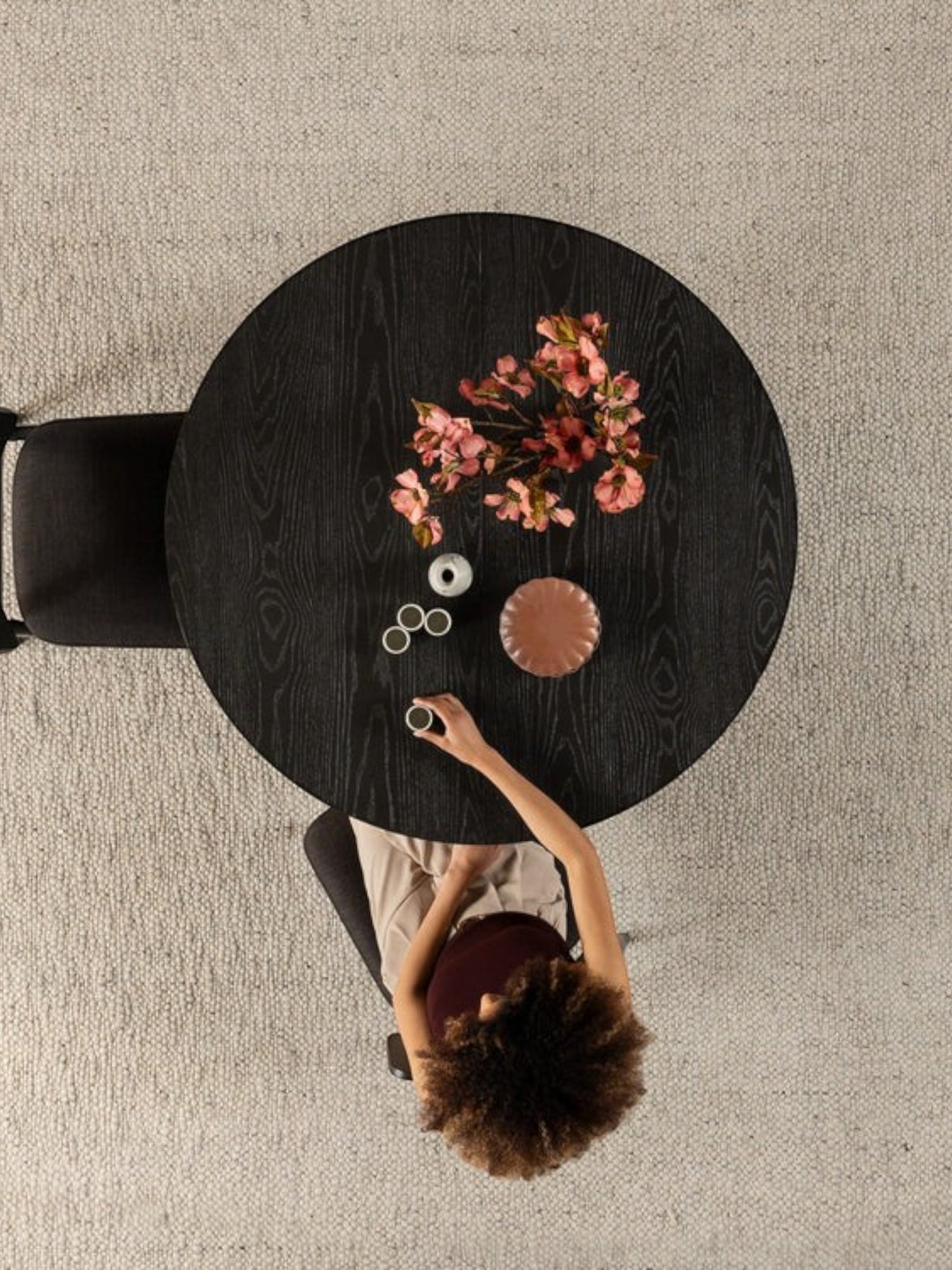 Table ronde en bois noir fumé TOCO Meubles avec fleurs roses et une femme buvant du café.