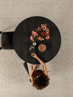 Table ronde en bois noir fumé TOCO Meubles avec fleurs roses et une femme buvant du café.